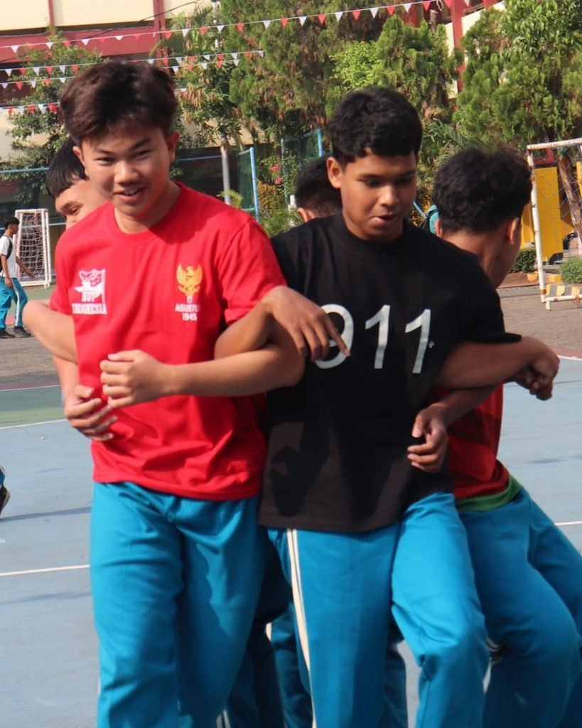 # Semarak Lomba 17-an HUT RI ke-81 di SMK Yadika 5 Pondok Aren: Tawa, Strategi, dan Jiwa Sportivitas Suasana lapangan SMK Yadika 5 Pondok Aren mendadak riuh rendah dan dipenuhi gelak tawa. Setelah khidmatnya upacara bendera memperingati HUT Kemerdekaan Republik Indonesia yang ke-81, kemeriahan berlanjut ke panggung utama perlombaan antarkelas. Tahun ini, deretan lomba unik dan menguji kekompakan seperti **Lomba 3 in 1, Bola Tampah, dan Lempar Balon** sukses menjadi magnet utama yang menyedot perhatian seluruh warga sekolah. ### **1. Aksi Seru Lomba 3 in 1: Uji Konsentrasi dan Kekompakan** Arena pertama langsung memanas lewat perlombaan *3 in 1*. Lomba estafet gokil ini menuntut setiap peserta didik untuk menyelesaikan tiga tantangan berbeda dalam satu paket rute: berjalan cepat sambil membawa kelereng di sendok, memecahkan balon dengan tekanan tubuh, hingga memasukkan paku ke dalam botol. Terpancar jelas raut wajah penuh konsentrasi sekaligus ekspresi kocak dari para peserta perwakilan jurusan TKJ dan Akuntansi. Jatuh bangun peserta di atas lintasan justru mengundang sorak sorai dan gelak tawa dari barisan suporter pendukung kelas masing-masing. ### **2. Keseruan Bola Tampah: Menjaga Keseimbangan Penuh Drama** Bergeser ke tengah lapangan, perlombaan *bola tampah* tak kalah menyita perhatian. Menggunakan tampah anyaman bambu, para peserta harus berjalan zig-zag melewati rintangan sambil membawa bola di atasnya tanpa boleh dipegang tangan. Angin sepoi-sepoi di area Pondok Aren seolah ikut menguji keseimbangan bola yang hampir jatuh. Teriakan dukungan *βAyo, pelan-pelan! Jangan sampai jatuh!β* membahana dari pinggir lapangan, menciptakan atmosfer kebersamaan yang begitu hangat di antara para siswa dan guru. ### **3. Pecahnya Tawa di Lomba Lempar Balon Air** Puncak keceriaan hari itu ditutup dengan *lempar balon* air yang basah dan penuh kejutan. Berpasangan saling berhadap-hadapan dengan jarak yang terus bertambah jauh setiap rondenya, para siswa harus melempar dan menangkap balon berisi air tanpa membuatnya pecah terlalu dini. Kegagalan demi kegagalan berbuah air yang tumpah membasahi seragam olahraga, memicu gelak tawa lepas tanpa sekat antarkelas. Di sinilah nilai kerja sama, strategi, dan kepercayaan antarteman diuji secara nyata. Melalui deretan lomba kreatif ini, perayaan kemerdekaan ke-81 di SMK Yadika 5 Pondok Aren bukan sekadar ajang mencari juara, melainkan wadah untuk merajut kebersamaan, melatih jiwa kepemimpinan yang sportif, dan menanamkan kenangan manis masa-masa putih abu-abu. *Dari tawa di lapangan, semangat kemerdekaan terus hidup di hati generasi muda Yadika 5!*